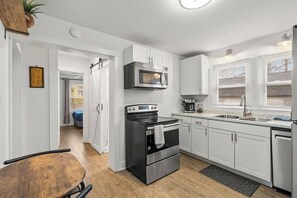 Una cocina moderna con gabinetes blancos, horno de acero inoxidable, microondas y cafetera.