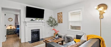 A living room with a fireplace, a sofa, a coffee table, and a television mounted on the wall.
