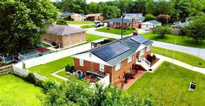 Ein Wohngebiet mit Häusern, eines davon mit einer Solaranlage auf dem Dach, umgeben von viel Grün und blauem Himmel.