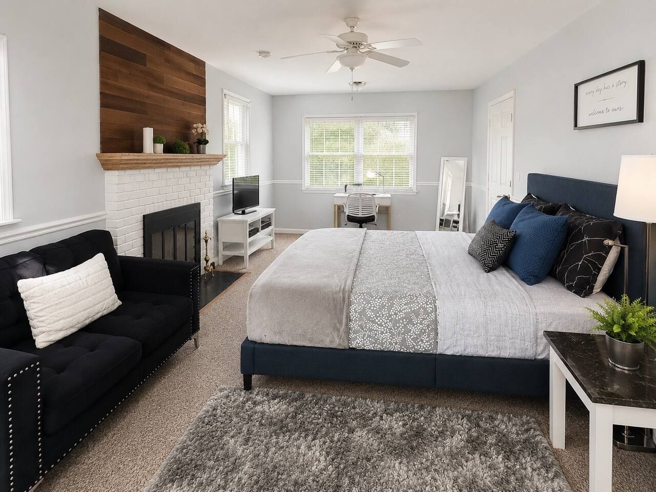 A bedroom with a bed, a black sofa, a desk, a fireplace, and a ceiling fan.