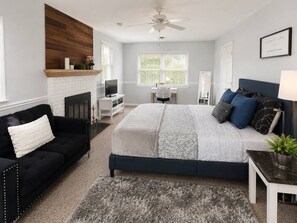 A bedroom with a bed, a black sofa, a desk, a fireplace, and a ceiling fan.