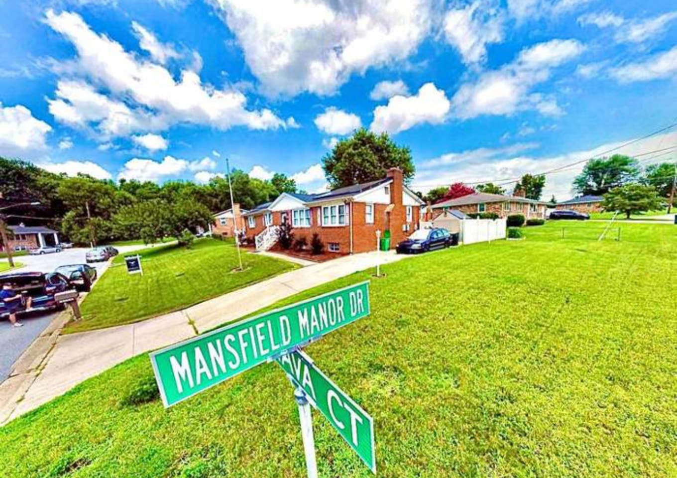 Una esquina residencial con una casa, un césped y una señal de calle que indica Mansfield Manor Dr.