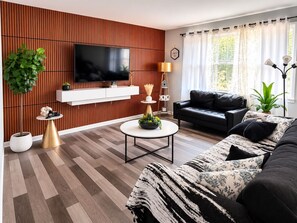 Una sala de estar moderna con un televisor de pantalla plana, un sofá de cuero negro, una mesa de centro redonda y una pared de acento de madera.