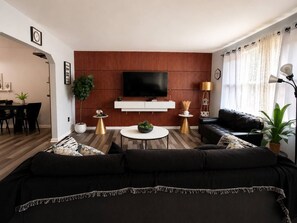 A modern living room with a black sofa, a white coffee table, and a flat-screen TV mounted on a wooden wall.