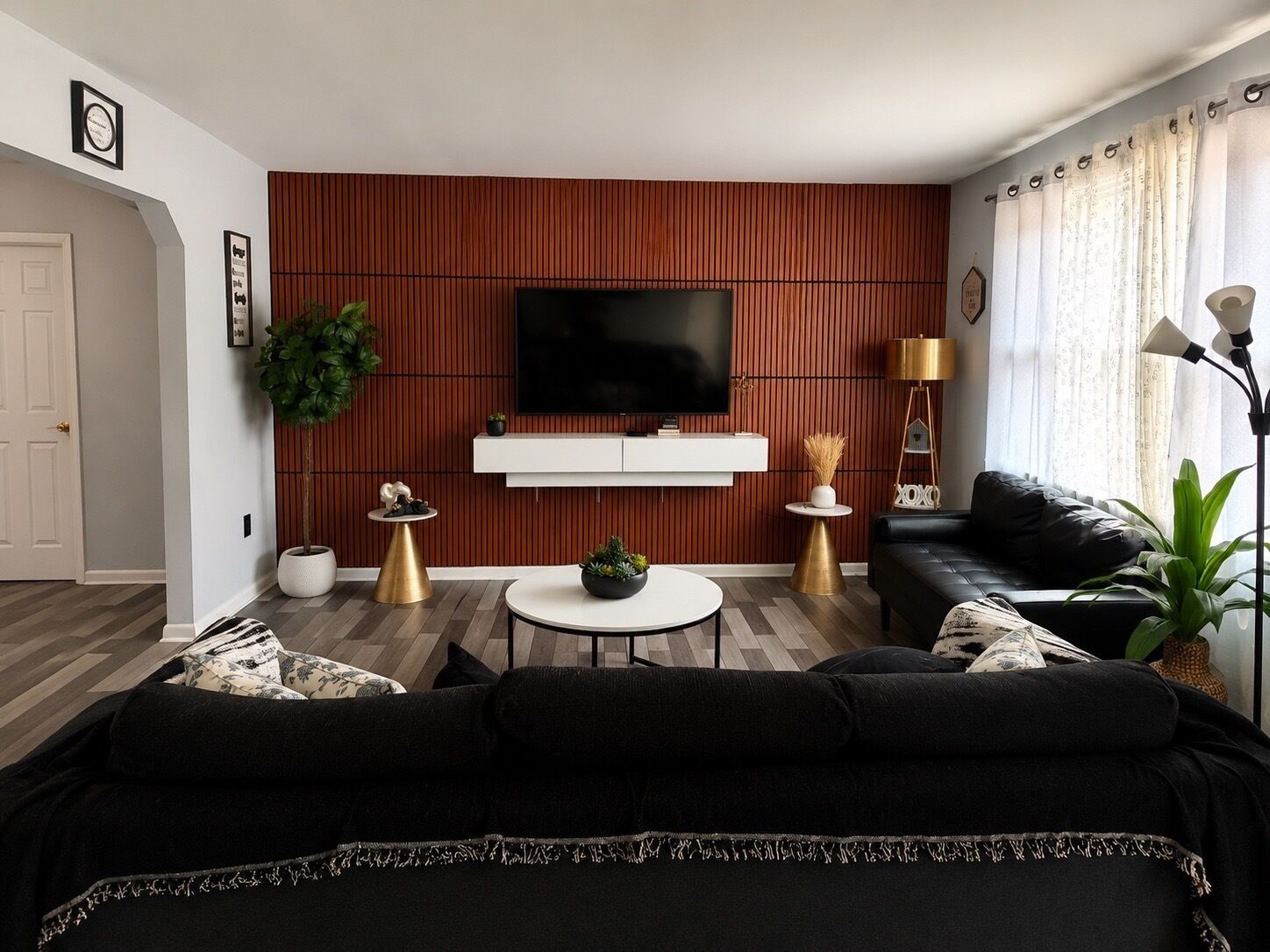 A modern living room with a flat-screen TV, a black leather sofa, a coffee table, and a wooden accent wall.