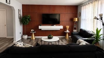 A modern living room with a flat-screen TV, a black leather sofa, a coffee table, and a wooden accent wall.