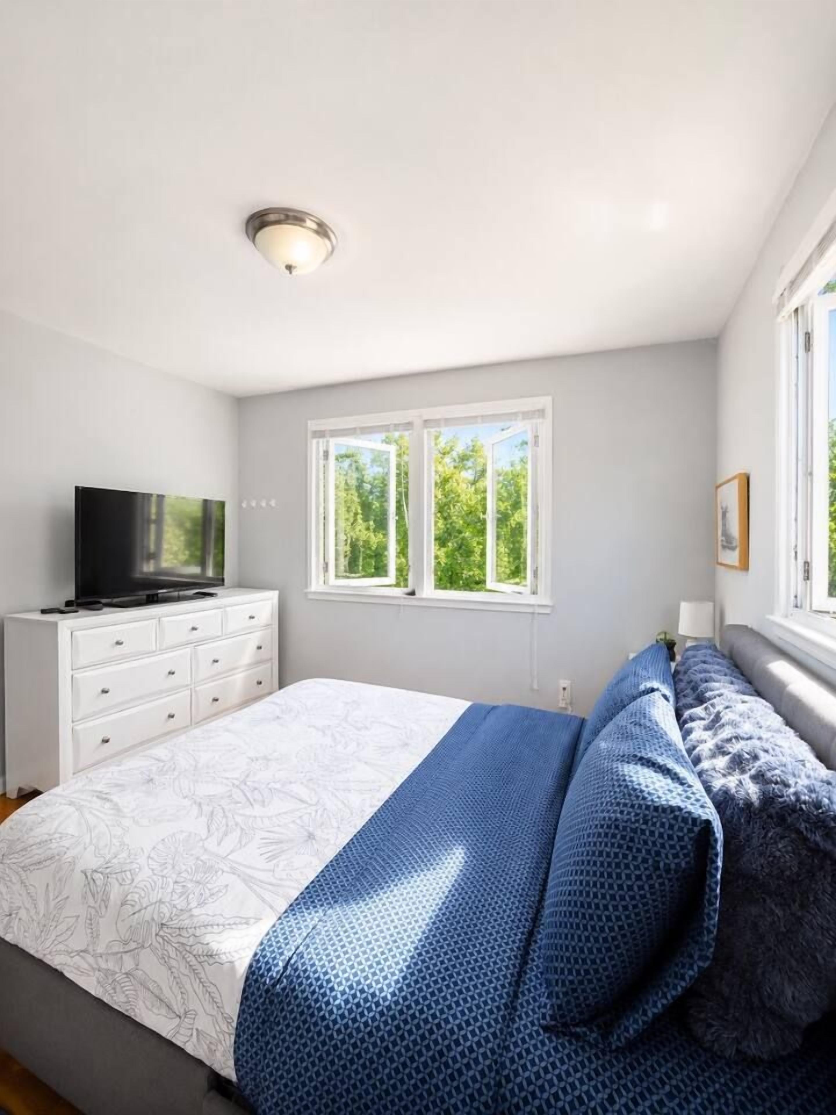 Une chambre à coucher avec un lit, un téléviseur posé sur une commode et une fenêtre donnant sur des arbres.