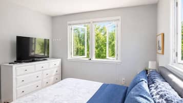 Une chambre à coucher avec un lit, un téléviseur posé sur une commode et une fenêtre donnant sur des arbres.