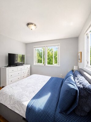 Une chambre à coucher avec un lit, un téléviseur posé sur une commode et une fenêtre donnant sur des arbres.