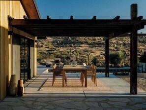 Une terrasse extérieure dotée d’une pergola, d’une table avec des chaises et offrant une vue sur un paysage vallonné.