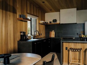A modern kitchen with wooden cabinetry, a black countertop, and a built-in stove. - Secluded Retreat | Two Homes, Pool + Firepit (Yucca Valley)
