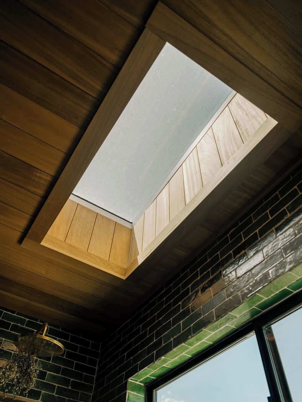Une lucarne dans une pièce dont le plafond est recouvert de panneaux de bois et un des murs est en briques.