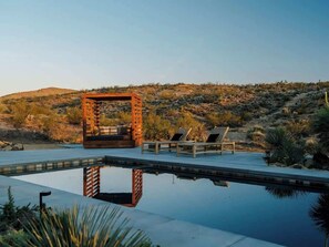 A pool area with a wooden pergola, lounge chairs, and a desert landscape in the background. - Secluded Retreat | Two Homes, Pool + Firepit (Yucca Valley)