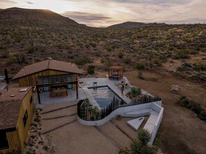 A desert landscape with a modern house featuring a swimming pool and outdoor seating. - Secluded Retreat | Two Homes, Pool + Firepit (Yucca Valley)