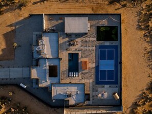 An aerial view of a residential property with a swimming pool, outdoor seating area, and a tennis court.