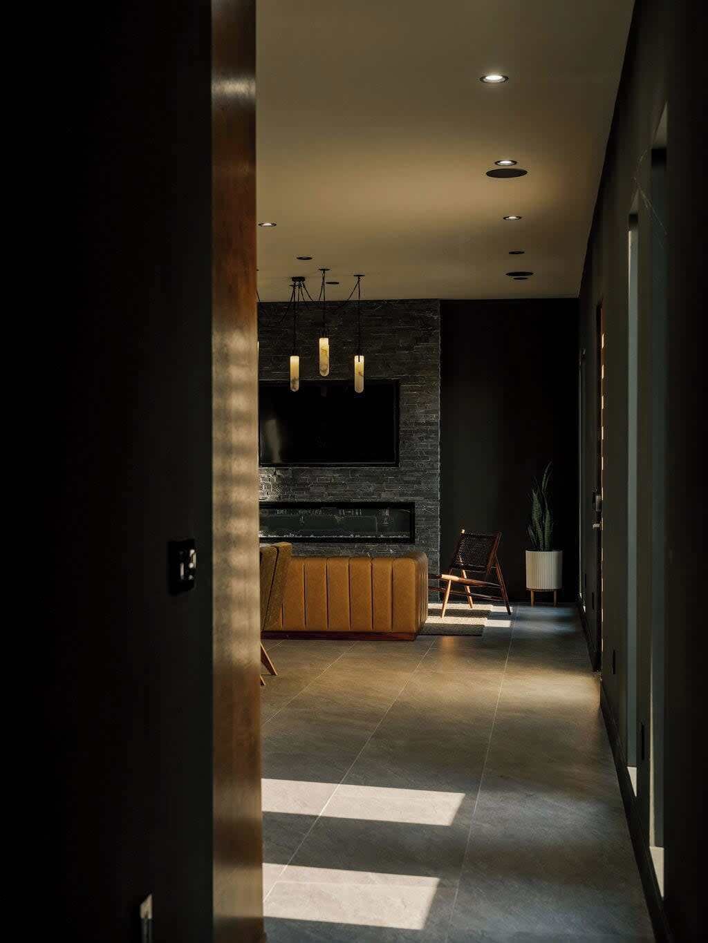 Un intérieur moderne avec un mur aux teintes sombres, un banc en bois et un téléviseur à écran plat fixé au-dessus.