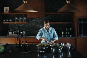 A person preparing food in a kitchen with marble countertops, wooden cabinets, and pendant lighting.