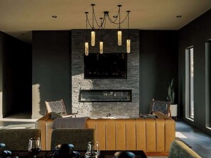 A modern living room with a sofa, a fireplace, and a television mounted on a stone wall. - Resort Pool | Pickleball, Sauna + Panoramic Views (Joshua Tree)
