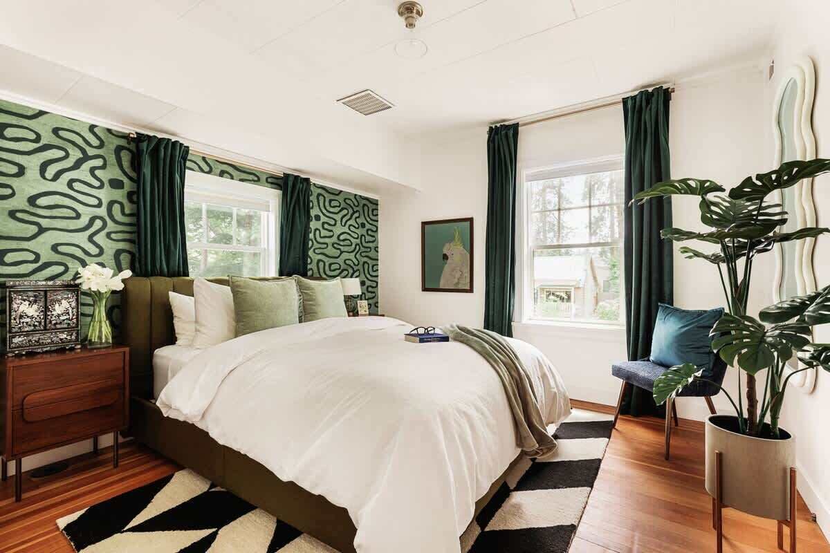 Un dormitorio con cama, mesita de noche, cortinas, una ventana y una planta en maceta.