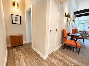 A hallway with a wooden bench, a closed door, and a dining area with orange chairs.