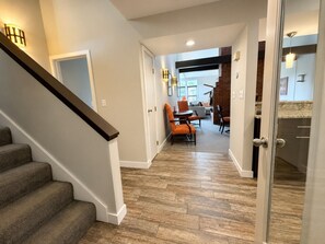 A hallway with a staircase, a dining area with chairs, and a kitchen area with a countertop.