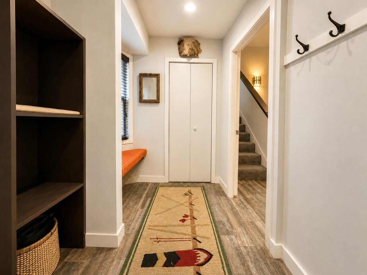 Un pasillo con piso de madera, un banco, una puerta y una escalera.