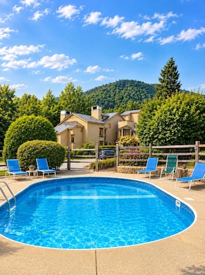 Ein Pool mit Liegestühlen, einem Holzzaun und einem Berg im Hintergrund.