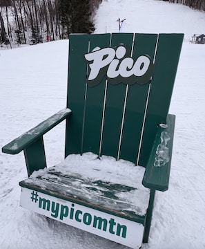Uma cadeira Adirondack verde com uma placa que diz 'Pico' e uma hashtag '#mypicomtn' no assento.