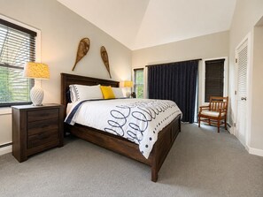A bedroom with a bed, nightstand, chair, and decorative wall pieces.
