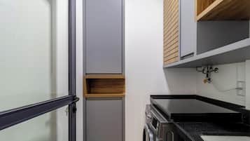 Una cucina compatta con forno integrato, una piccola mensola in legno e un piano di lavoro nero.