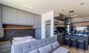 Un dormitorio moderno con cama, sofá y una pequeña zona de kitchenette.