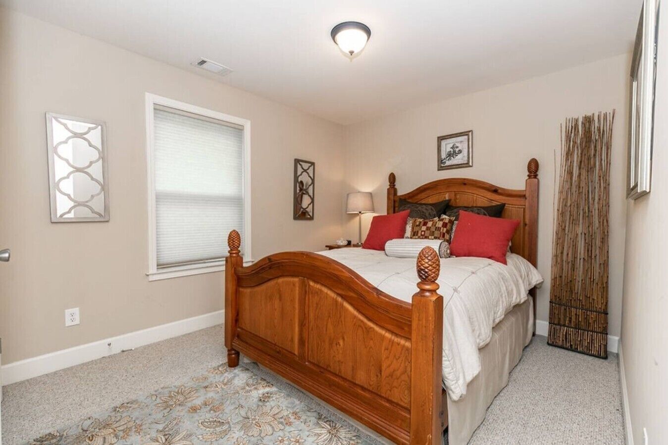 A bedroom with a wooden bed, a window with blinds, a bedside lamp, and a decorative wall piece.