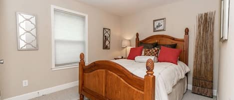 A bedroom with a wooden bed, a window with blinds, a bedside lamp, and a decorative wall piece.