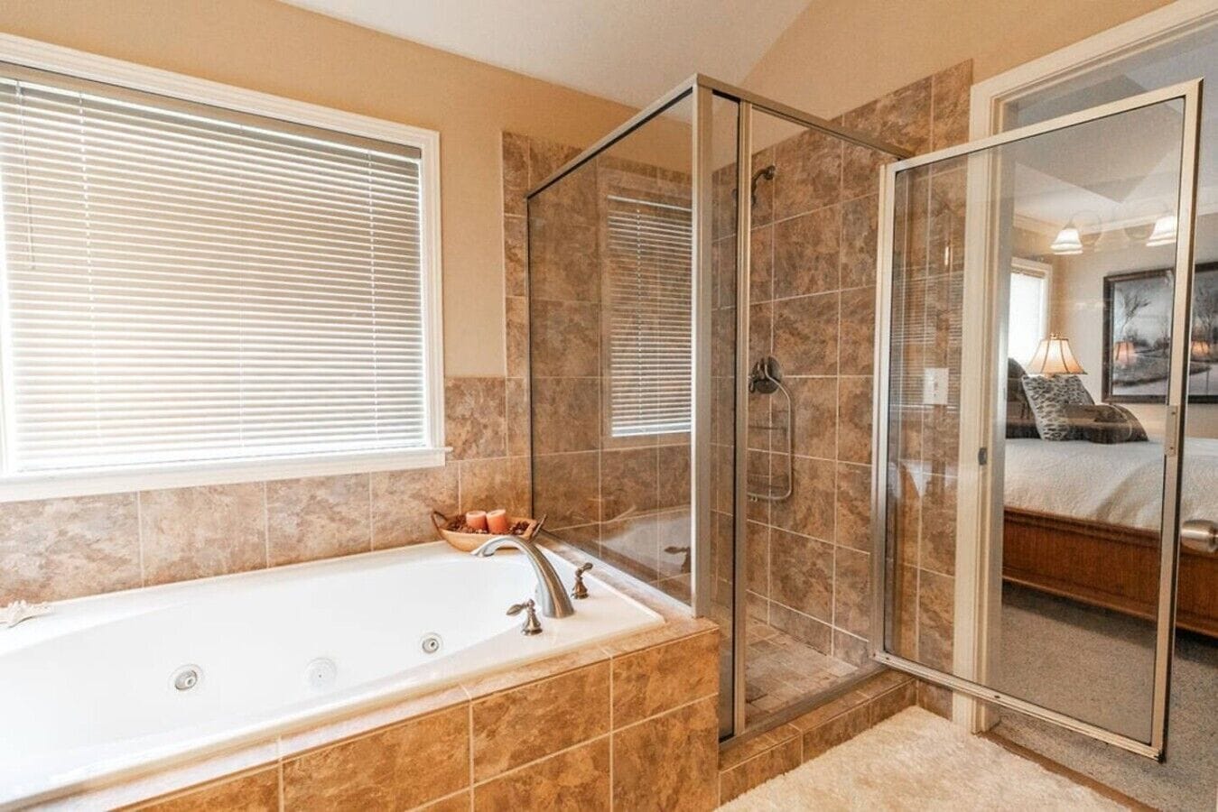 A bathroom with a glass-enclosed shower, a bathtub with a faucet, and a window with blinds.