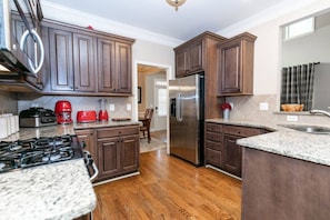 A modern kitchen with dark wood cabinets, granite countertops, a stainless steel refrigerator, and a gas stove. - Family Escape | Movie/Game Lounge, Near Downtown (Mableton)