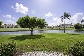 A well-maintained grassy area with a small tree and a body of water, likely a pond, with buildings in the background. - NEW Island Living at Isla Del Sol | Ground Floor 2BR/2BA Getaway (Isla Del Sol)