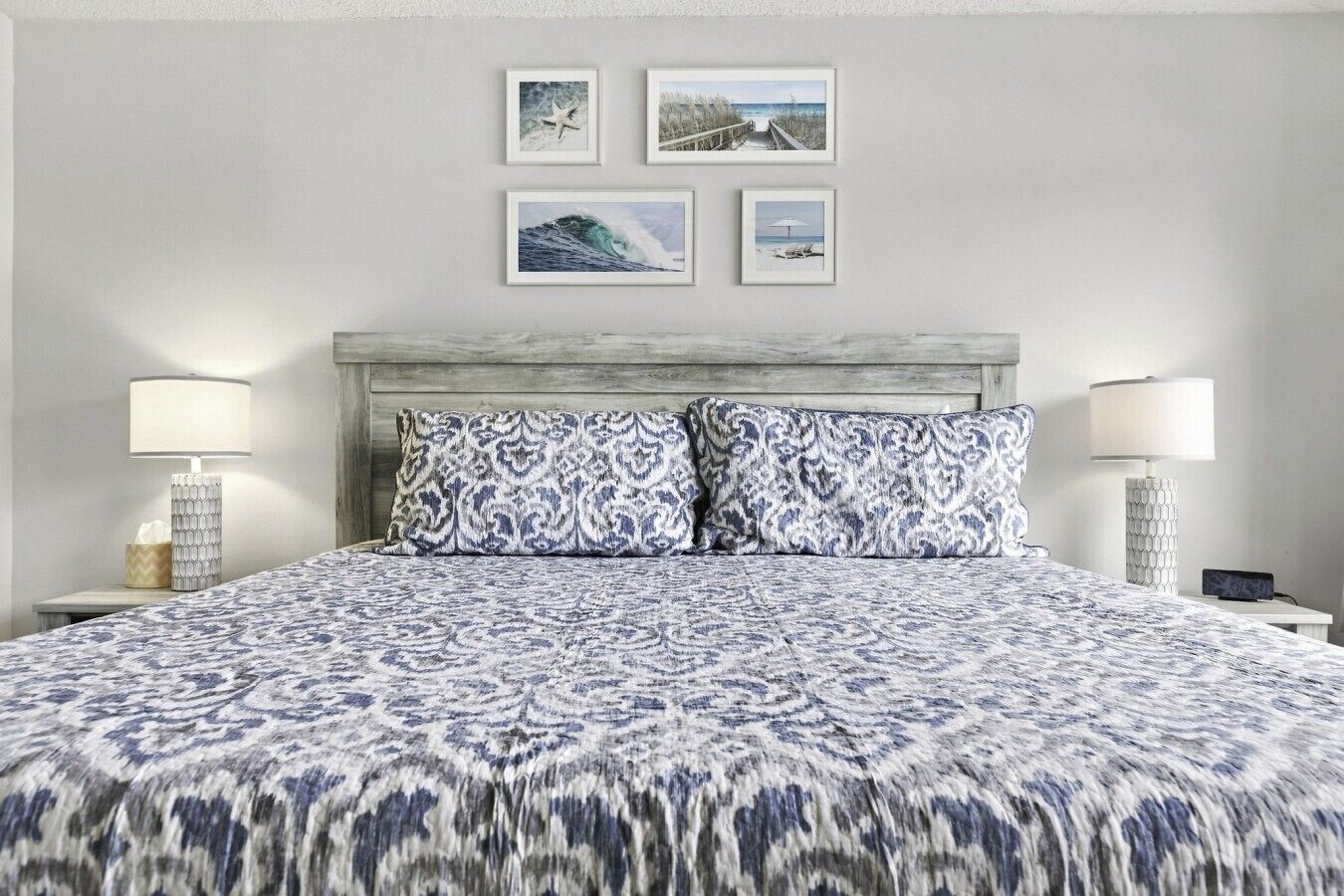 Ein Hotelzimmer mit einem Bett, zwei Nachttischlampen, einer Kopfteil und vier gerahmten Bildern an der Wand.