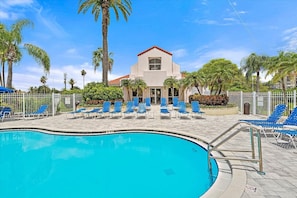 A swimming pool with blue lounge chairs and a building with a red roof in the background. - Island Living at Isla Del Sol | Ground Floor 2BR/2BA Getaway (Isla Del Sol)