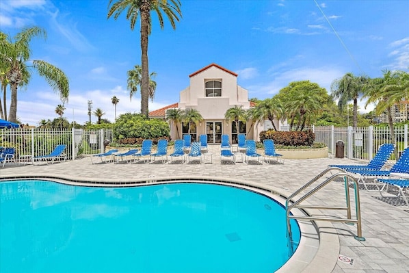 Ein Swimmingpool mit blauen Liegestühlen und ein Gebäude mit rotem Dach im Hintergrund.