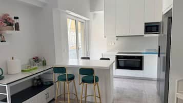 Eine moderne Küche mit weißen Schränken, einer zentralen Kochinsel mit Barhocker, einem Backofen und einer Mikrowelle.