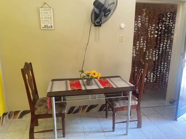 A dining table with a fan, chairs, and a vase with flowers.