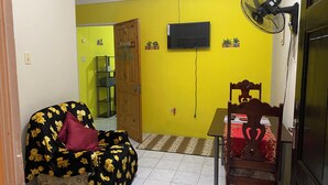 Quarto com sofá, mesa de jantar, televisão na parede e ventilador.