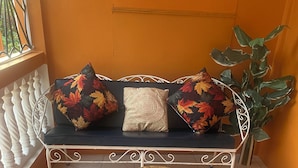 Canto de um quarto com um banco de metal branco, uma mesa de madeira redonda e um vaso com planta.
