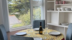 Ein Essbereich mit einem runden Tisch für vier Personen, Stühlen, einer Prosecco-Flasche und Blick auf Bäume durch das Fenster.