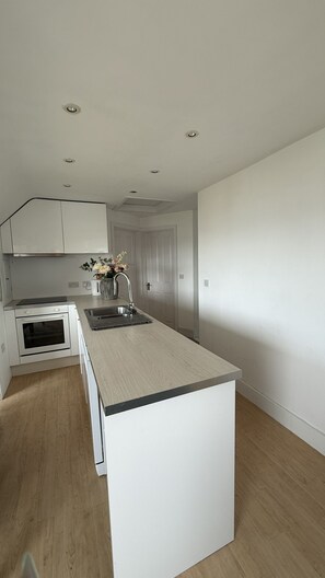 A modern kitchen with white cabinetry, a central island, and a built-in oven. - BellaVista 1B-Sleeps 4 in 2 Bedrooms (New Polzeath)