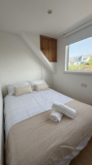 A bedroom with a bed, pillows, a window, and a wooden cabinet. - BellaVista 1B-Sleeps 4 in 2 Bedrooms (New Polzeath)