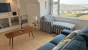Ein modernes Wohnzimmer mit einem blauen Sofa, einem Holztisch und einem Fernseher an der Wand.