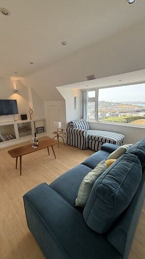 A modern living room with a blue sofa, a wooden coffee table, and a television on the wall. - BellaVista 1B-Sleeps 4 in 2 Bedrooms (New Polzeath)