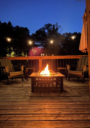 Eine Holzterrasse mit einem zentralen Feuerbereich, umgeben von Stühlen und Lichterketten.