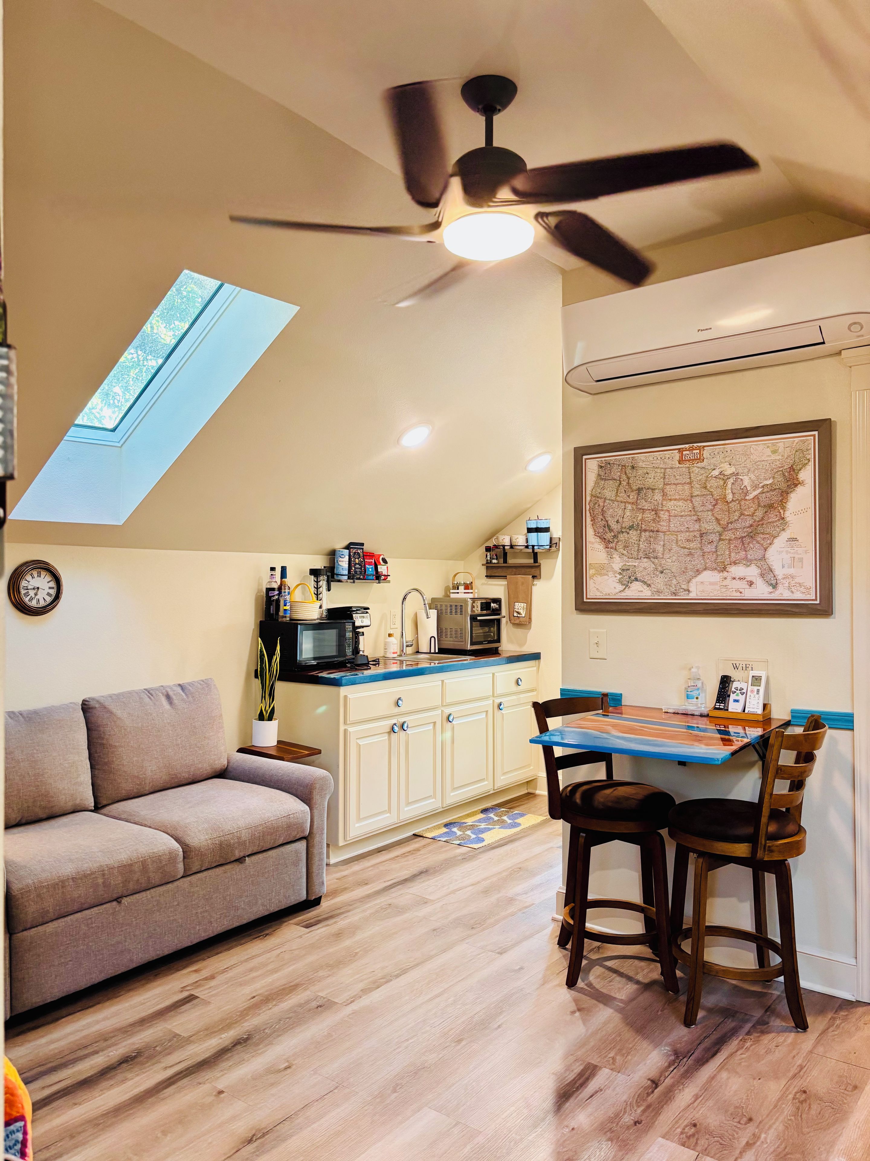 Une cuisine compacte avec un ventilateur de plafond, une table à manger avec des chaises, un canapé et une carte accrochée au mur.